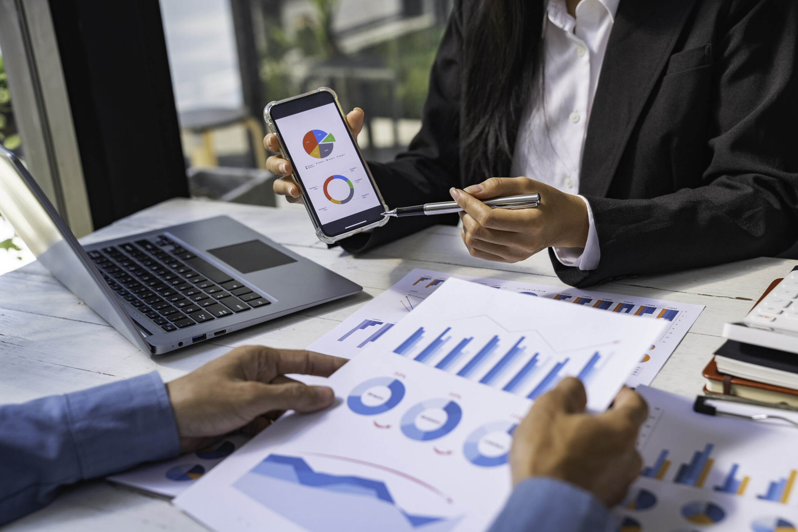 Two business people sit down to analyze financial data from earnings graphs showing the company's earnings to be presented at a meeting.